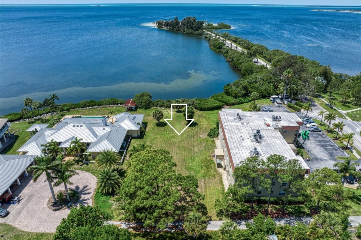 Vacant waterfront lot marked with arrow – A grassy open plot of land located between two buildings, pointing towards a scenic view of the bay and small island.