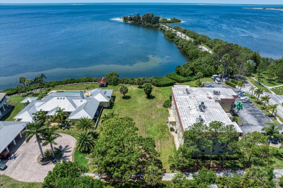 Vacant lot facing the bay between two buildings – A green, empty lot with direct waterfront access, bordered by two developed properties.