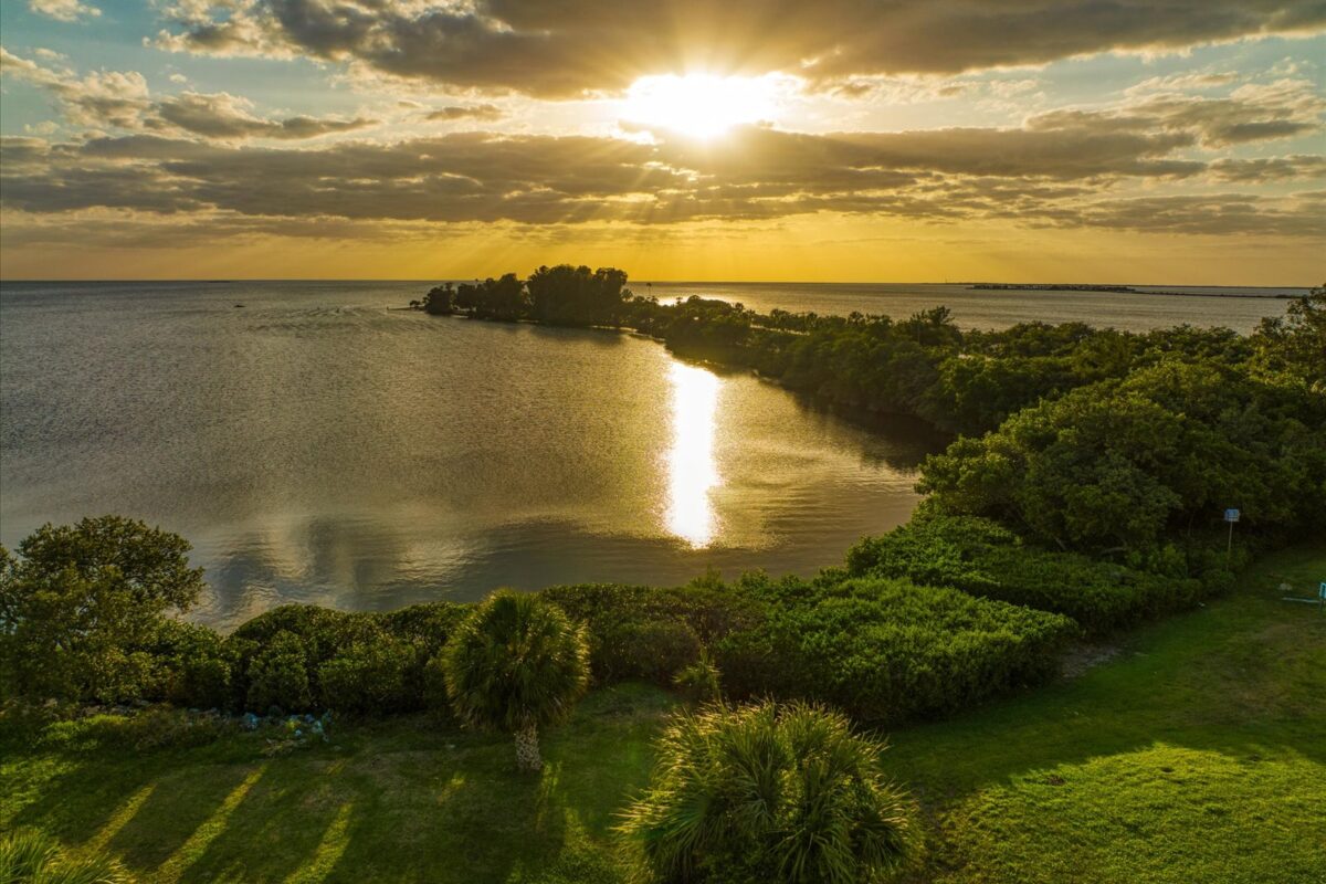 Sunset over calm coastal landscape – A picturesque sunset casting warm colors over a serene coastal area with lush greenery and distant islands.