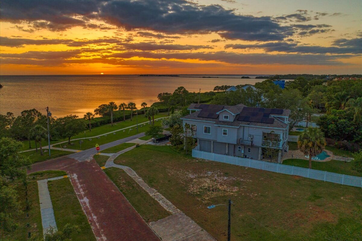 Neighborhood street at sunset near the bay – A peaceful residential area during sunset, with a house, paved street, and waterfront view under a colorful sky.