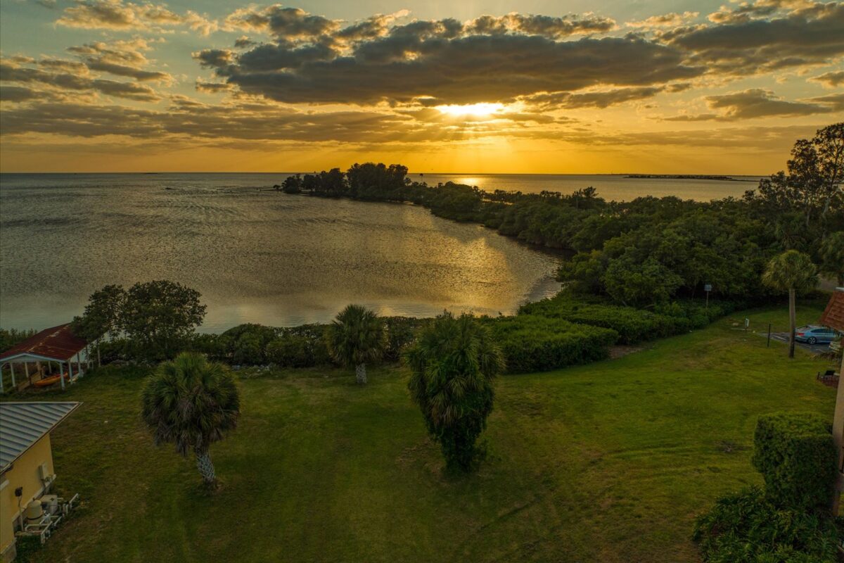 Sunset over calm coastal landscape – A picturesque sunset casting warm colors over a serene coastal area with lush greenery and distant islands.