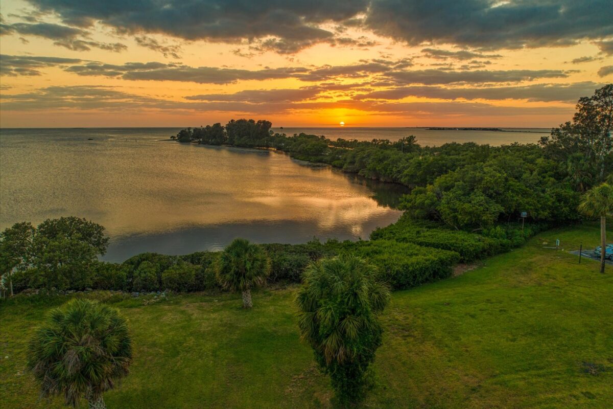 Sunset over calm coastal landscape – A picturesque sunset casting warm colors over a serene coastal area with lush greenery and distant islands.