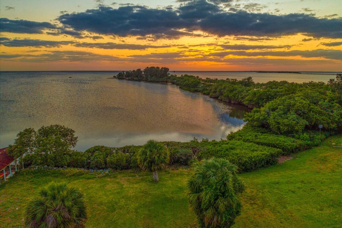 Sunset over calm coastal landscape – A picturesque sunset casting warm colors over a serene coastal area with lush greenery and distant islands.